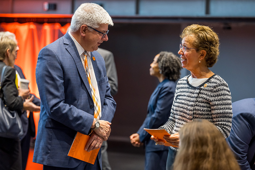 a man and a woman speak to each other in a room full of people