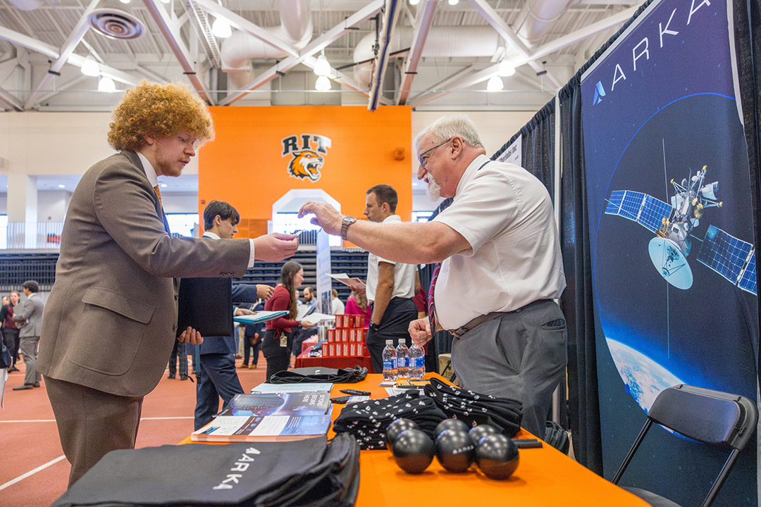 a student speaks to a man behind a table with a sign that says ARKA.