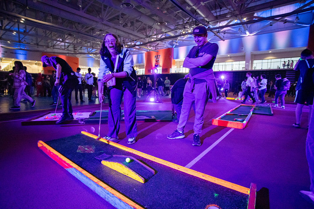 A man and woman are shown playing glow mini golf inside the Gordon Field House during Eclipsefest.