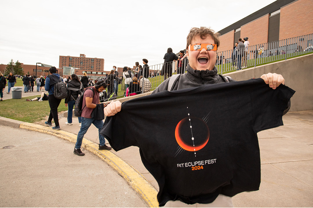a student is shown wearing eclipse glassews and smiling gleefully while displaying his eclipsefest shirt.