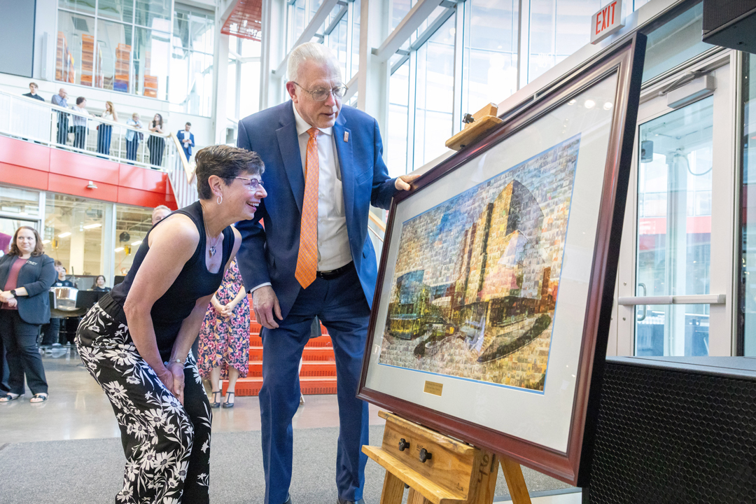 A man and a woman look at a framed piece of artwork