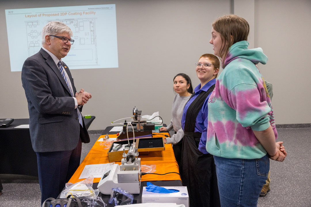 a man stands in front of a table speaking to students about a research project.