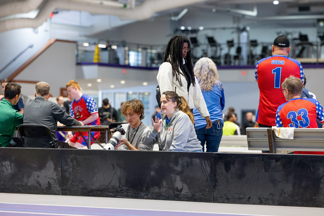 people are seated watching athletes in an interior gym environment.