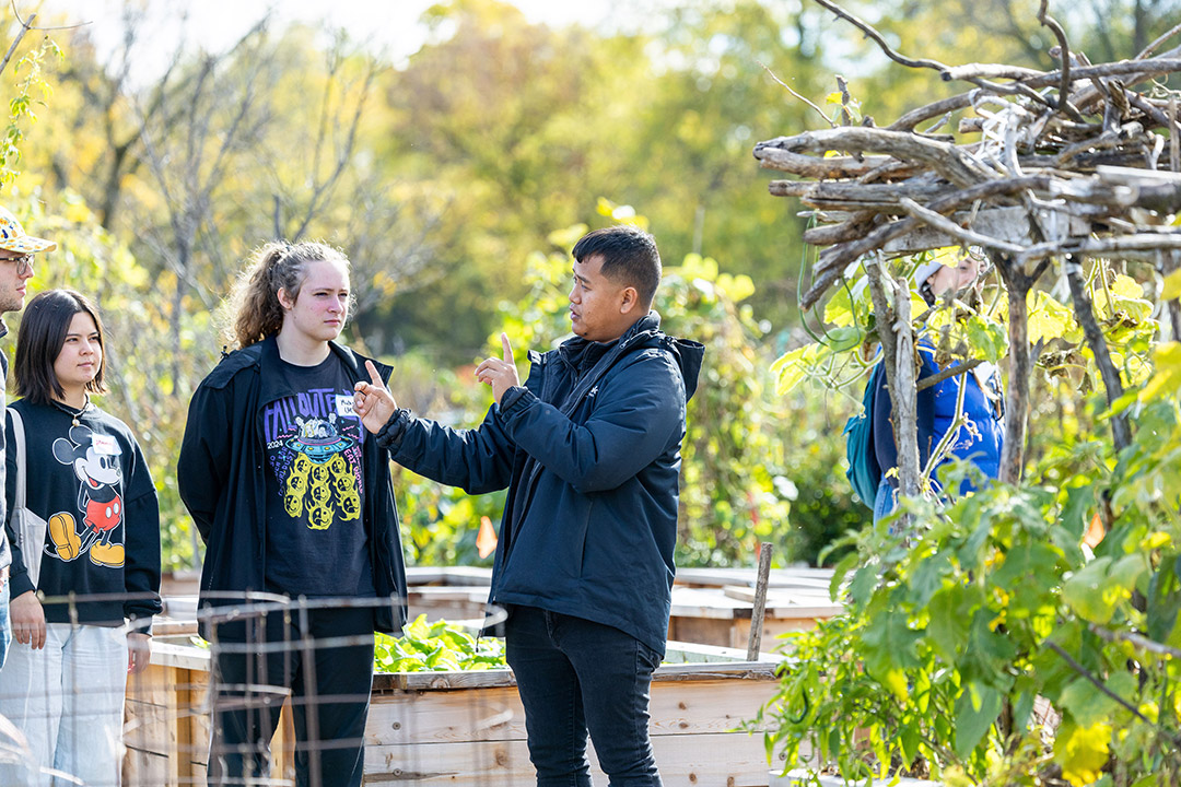 a man speaks to a group of people in a garden like area.