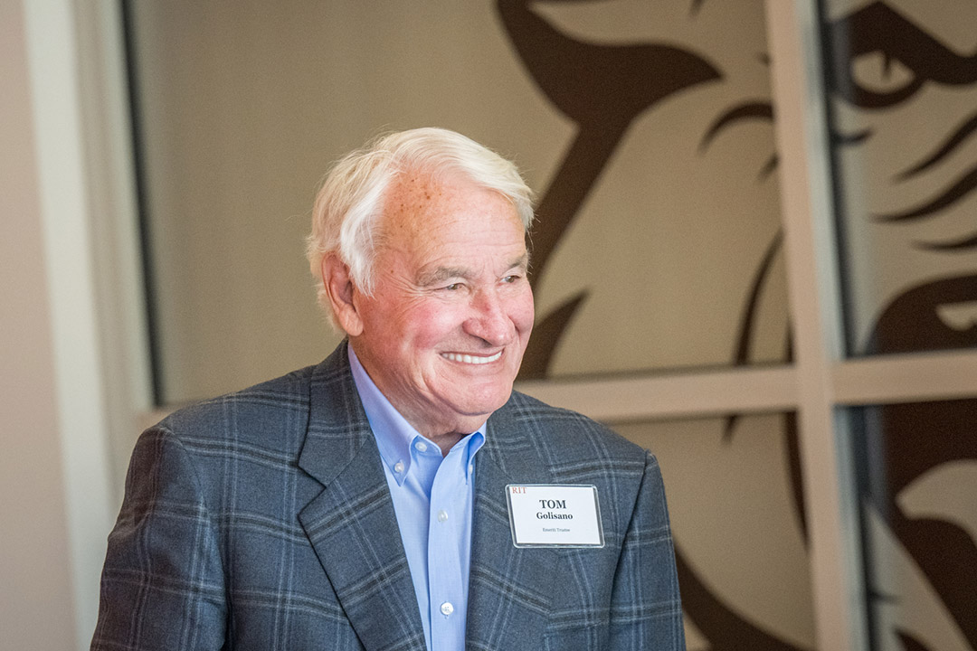 B. Thomas Golisano stands at a podium speaking to an unseen group of people.