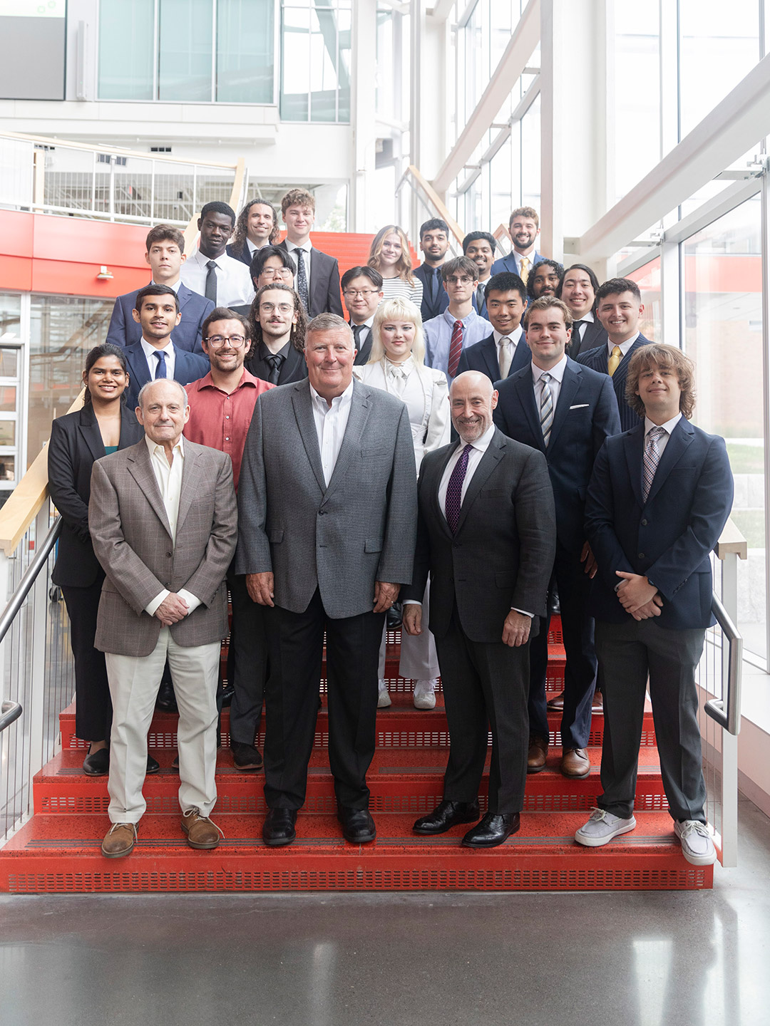 Group of people in business attire posing on red staircase inside modern building.
