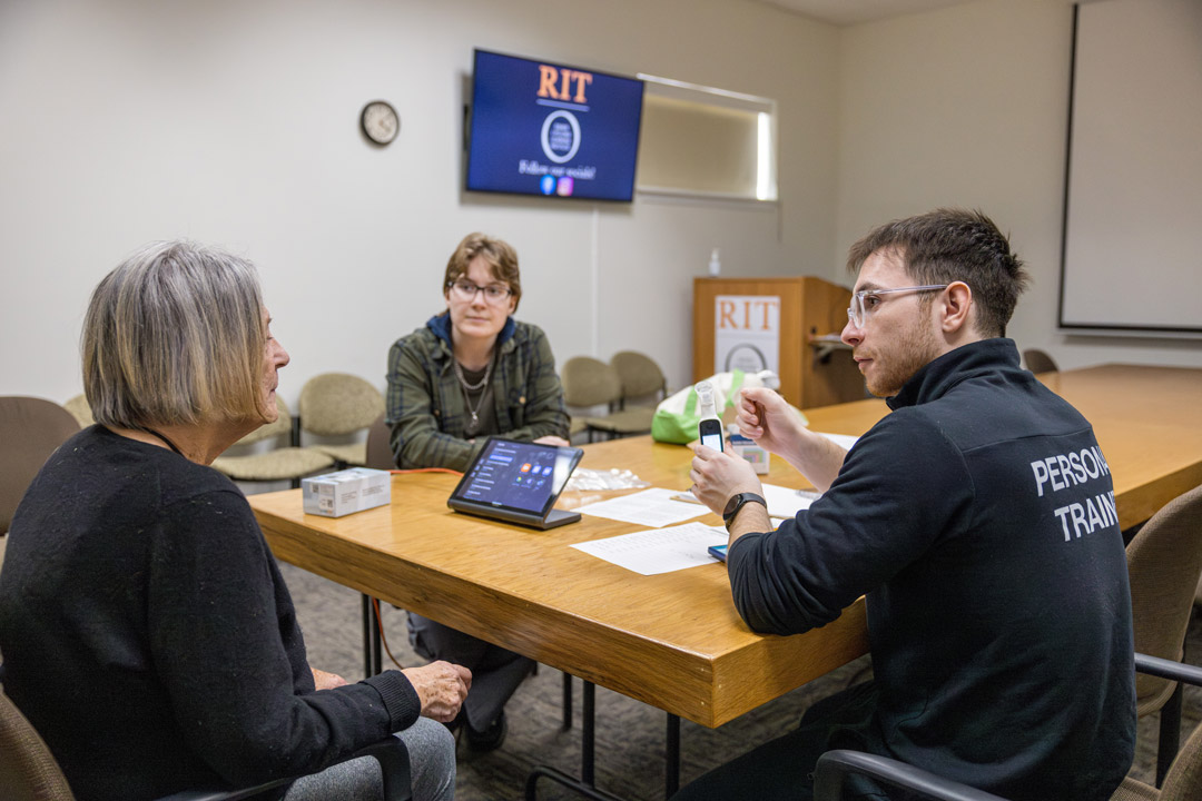 three people sit at a conference table in a classroom.