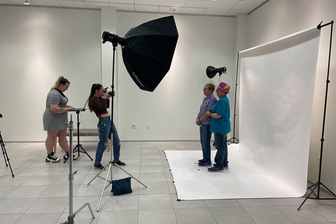 People stand with a camera in front of a backdrop with two other people