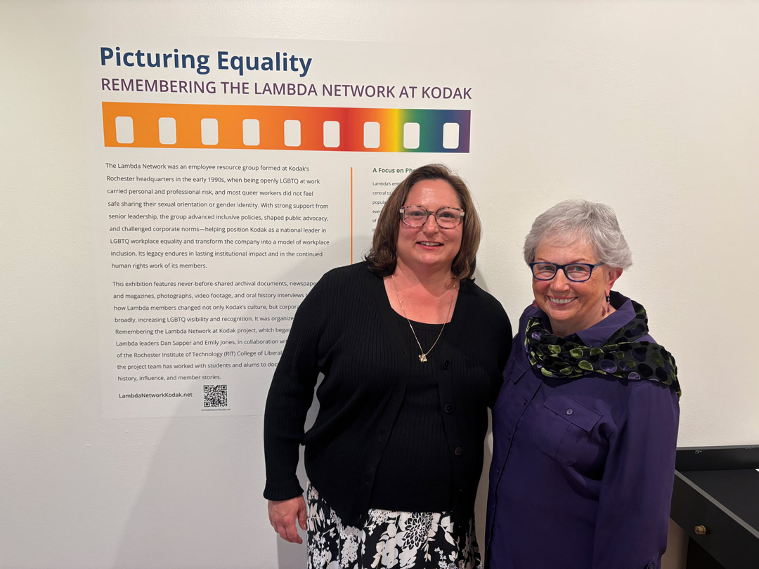 Two people pose in front of a wall sign announcing a museum exhibit