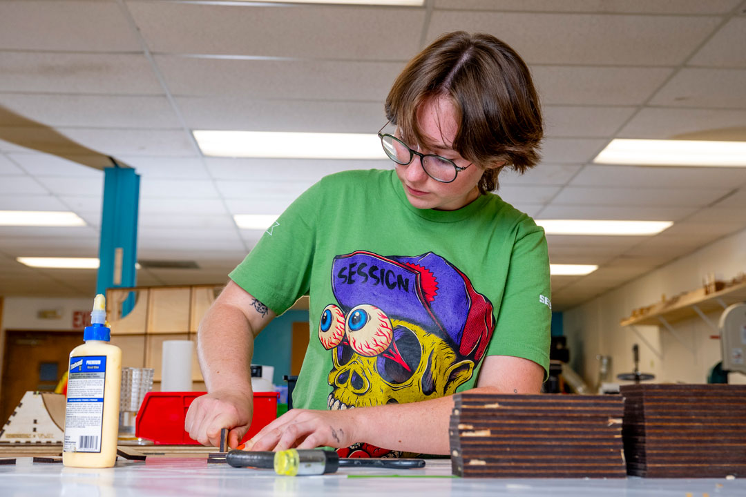 a college age person with shirt hair and glasses works on her fingerboarding project.