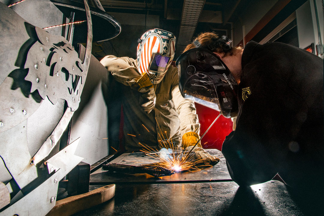 A student wears a welding mask as they weld metal
