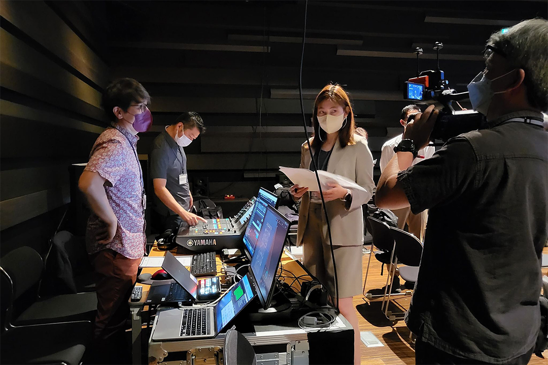 Four masked people sitting around a table covered with computer monitors and audio equipment