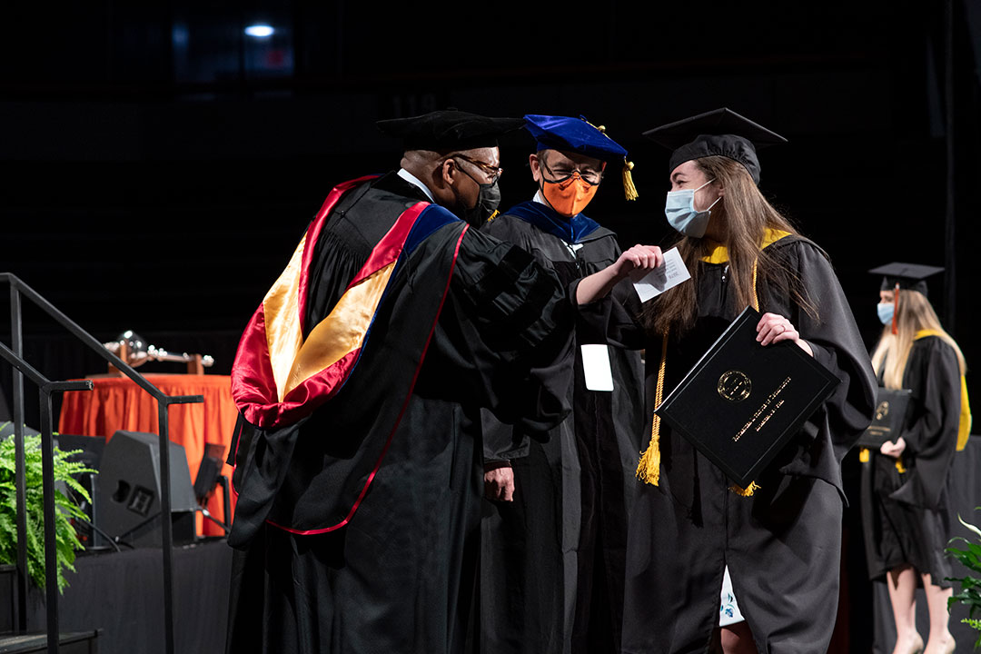 Graduate elbow-bumping faculty on stage during graduation.