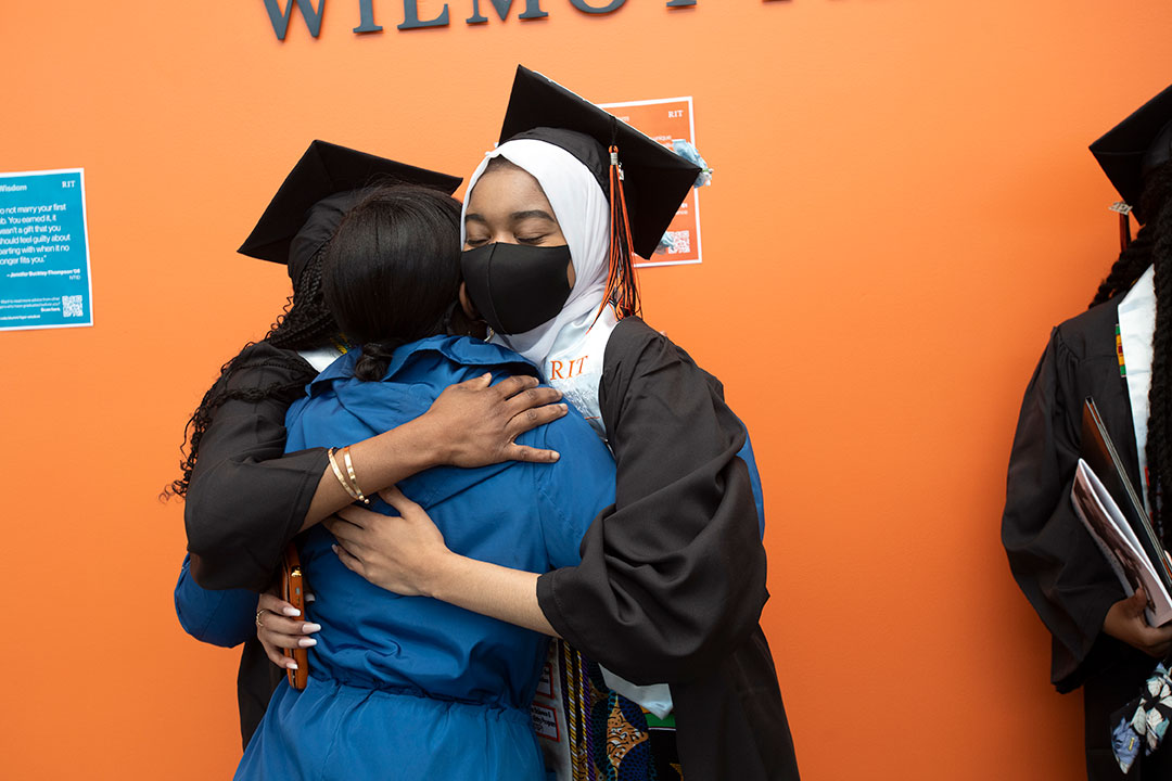 Student wearing graduation regalia hugging a family member.