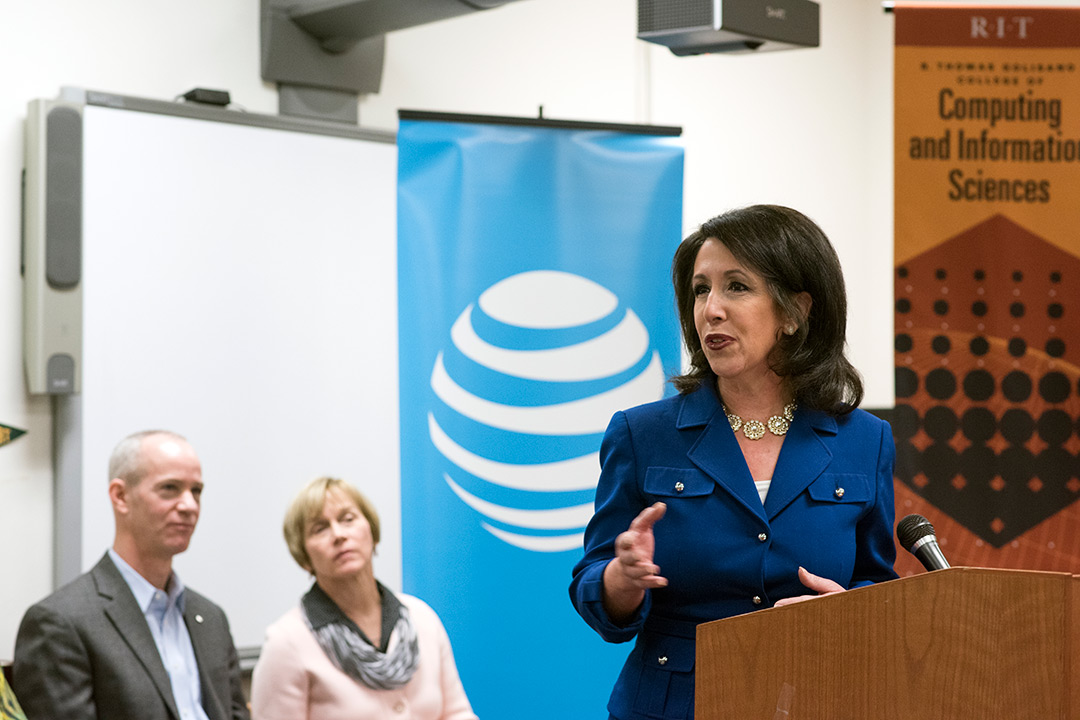 Woman speaks at podium as woman and man in background look on