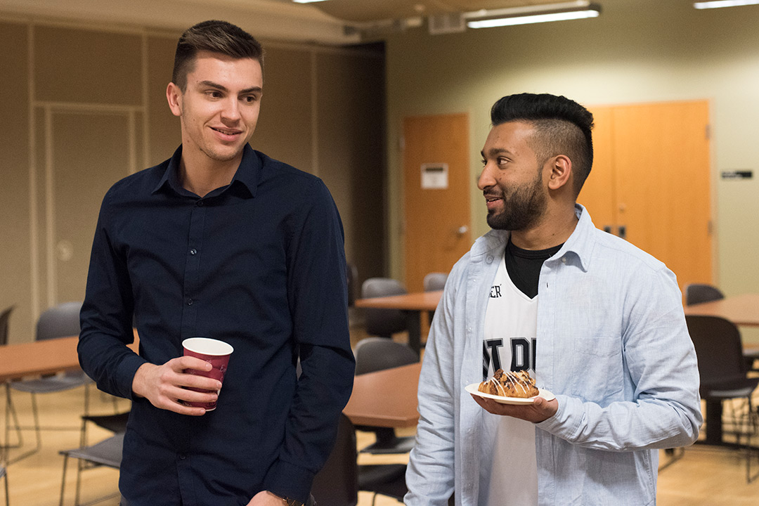 Two male students stand near each other holding refreshments