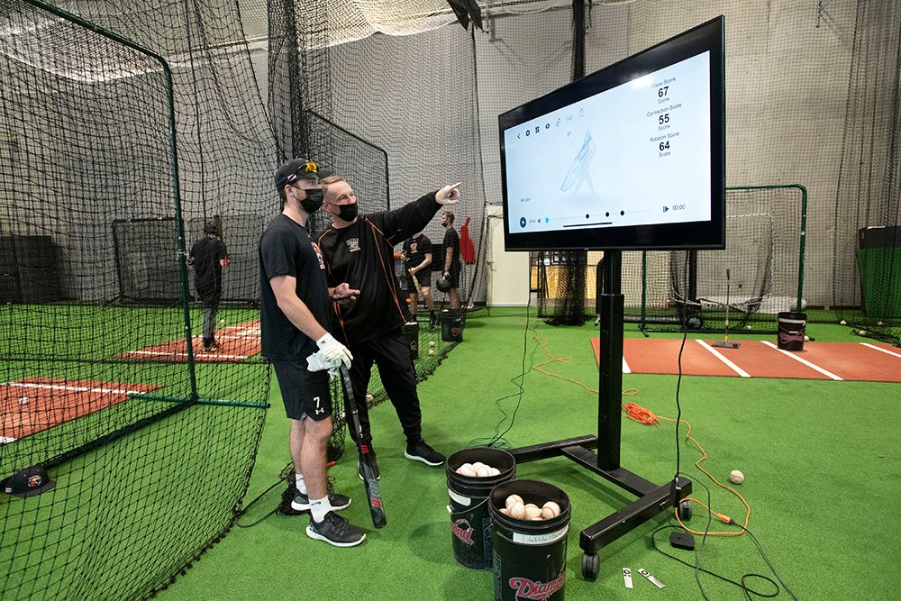 athlete and coach look at TV screen displaying data about hitting a baseball.