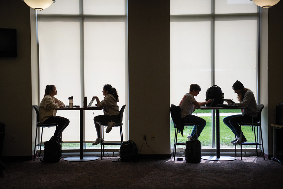 profile view of two pairs of college students sitting at high-top tables.