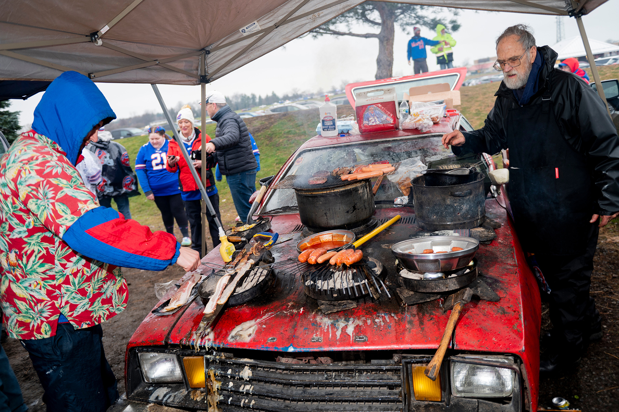 Tailgaters grill on the hood of a car.