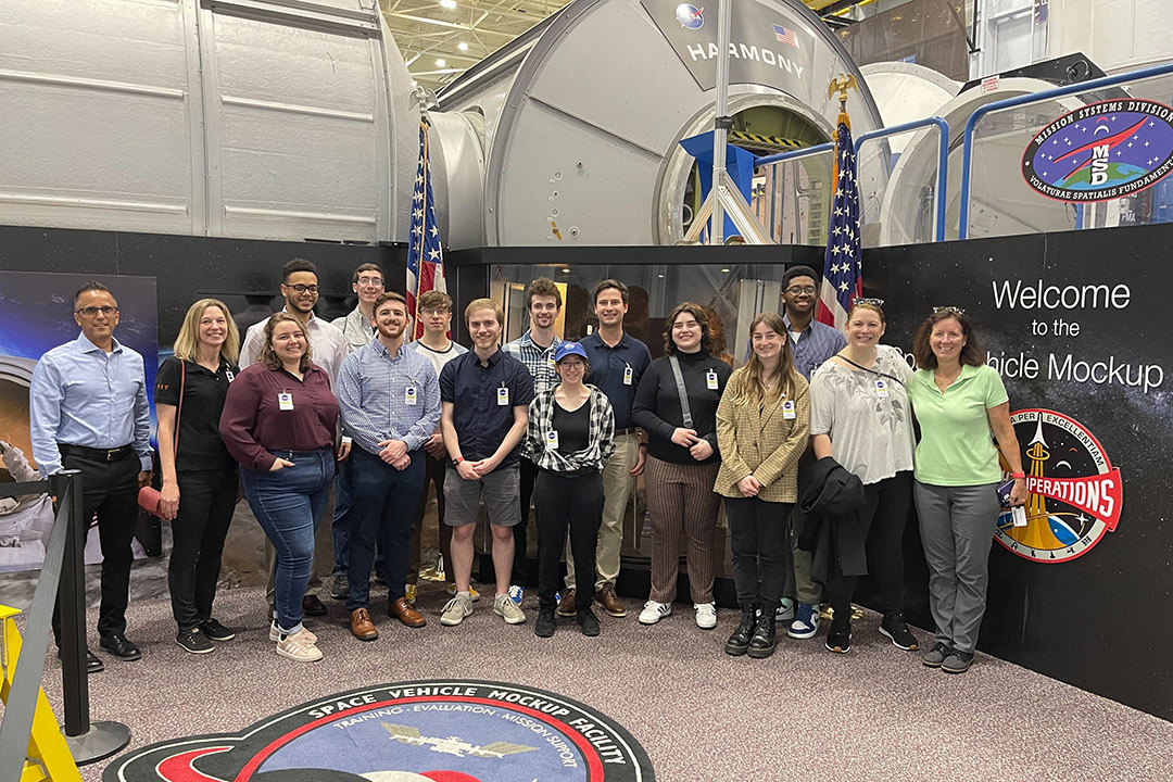 16 people standing in the Space Vehicle Mockup Facility.
