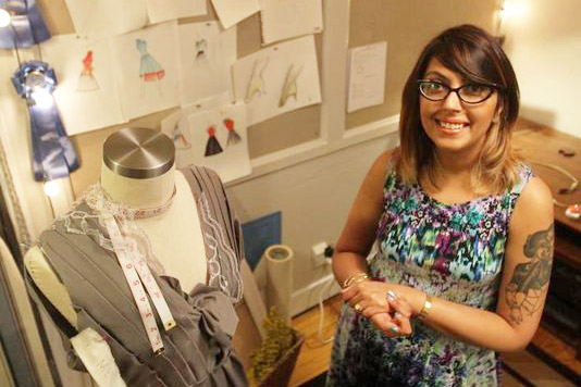 Woman stands next to mannequin wearing dress she is designing.