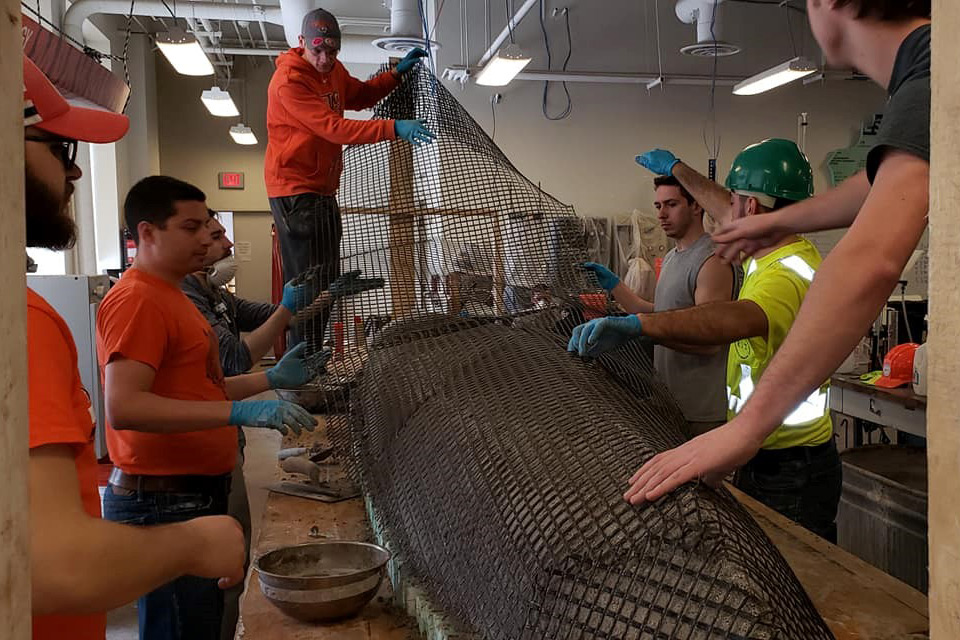 Students lay mesh covering to overturned canoe structure.