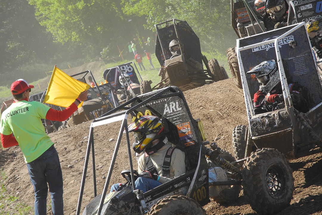 volunteer waving a yellow flag as baja cars drive through a racecourse.