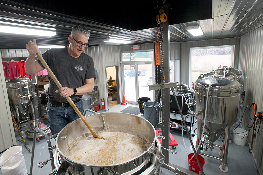 man stirring large vat of beer.