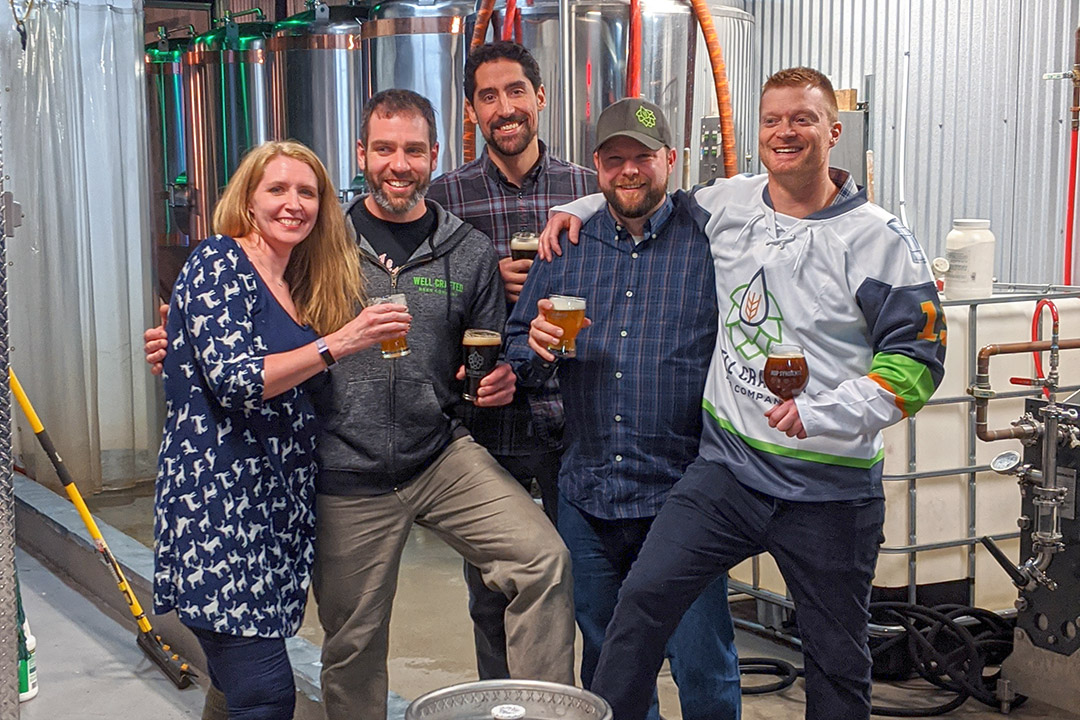 five people standing holding beers.