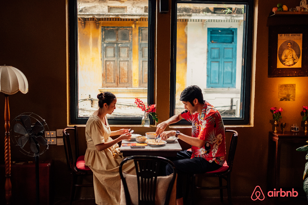Two people eat at a table in a photo for Airbnb.