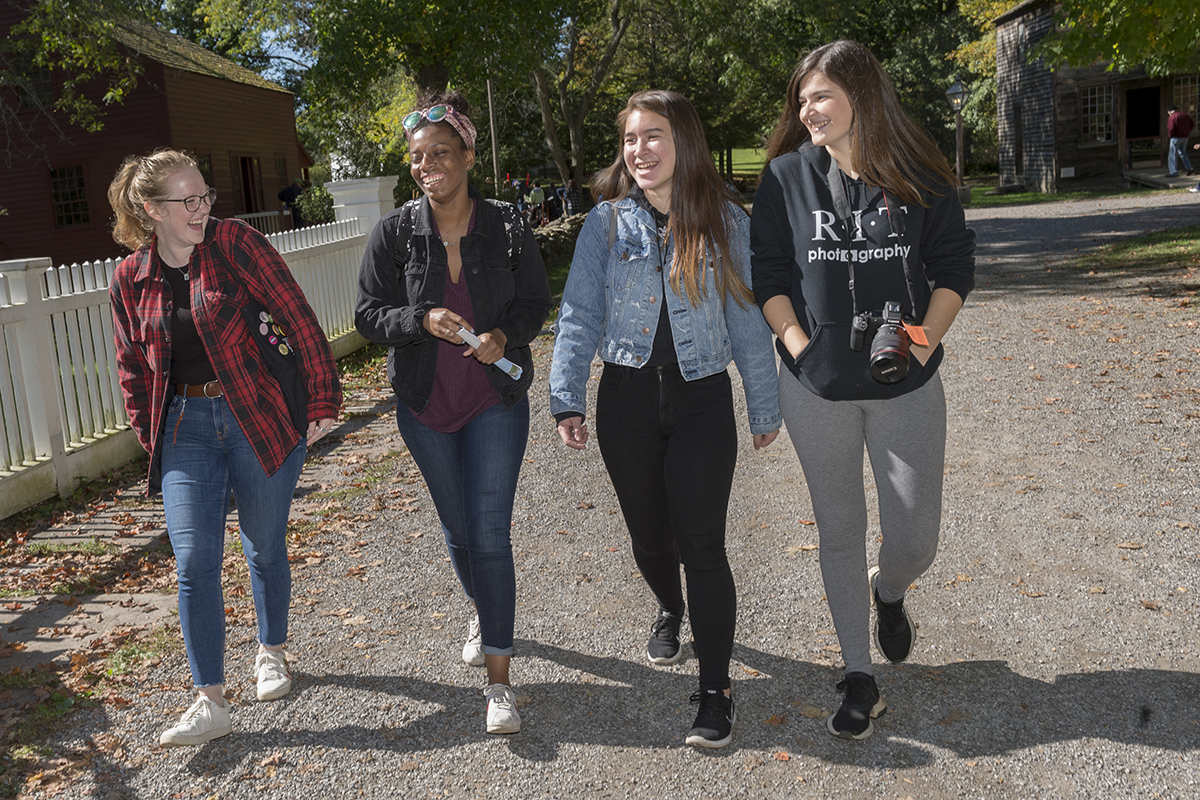 Four students walking and laughing at the Genesee Country Village and Museum's annual fall fair.