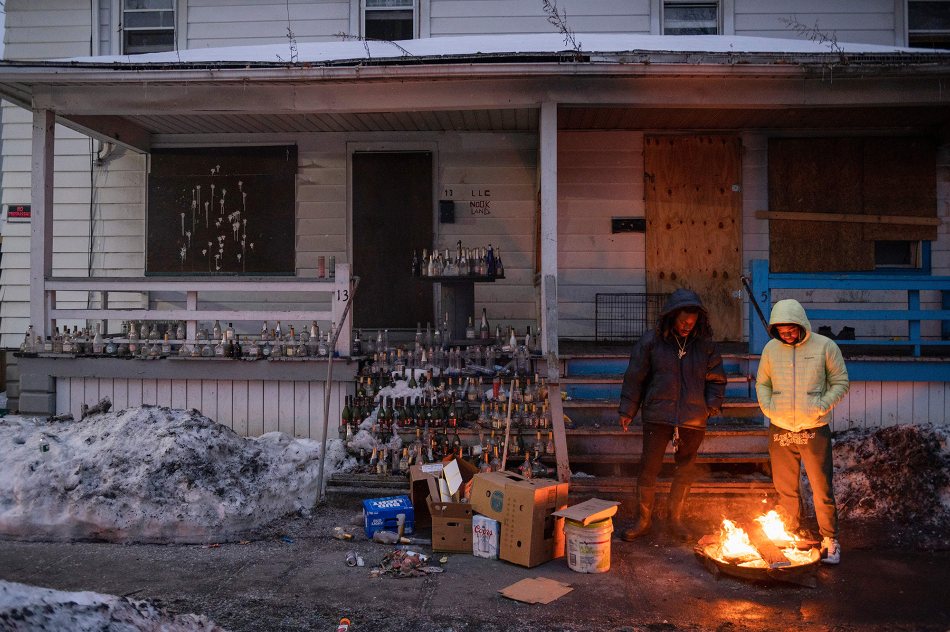 Two men sit outside with a lit fire pit.