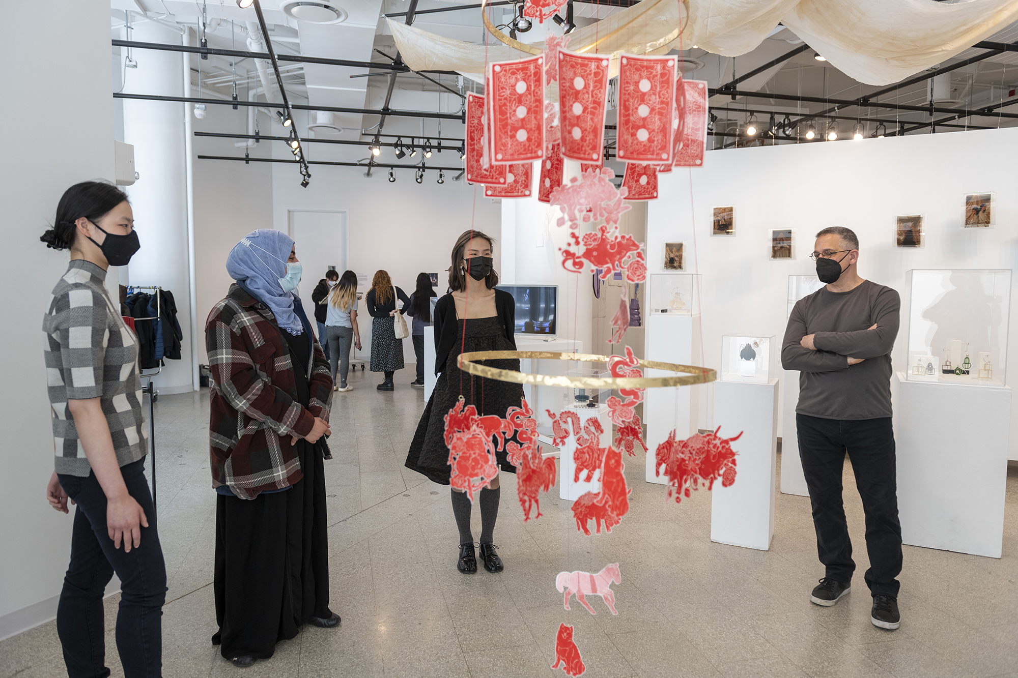 A group of people stand around an intricate piece of art that is suspended from a ceiling.