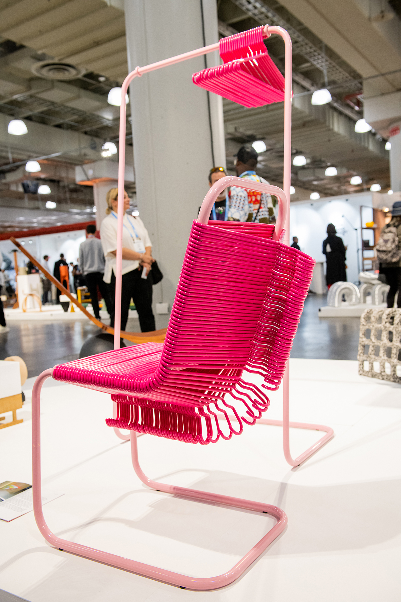 The Coat Check Chair sits on the WantedDesign floor next to a rack of coat hangers.