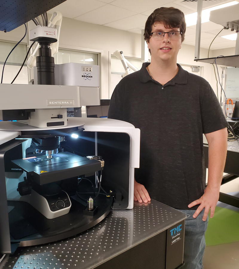 student standing next to microscope in lab