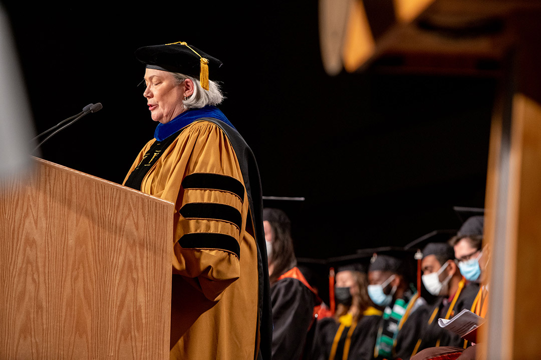 provost wearing graduation regalia speaking at a podium.