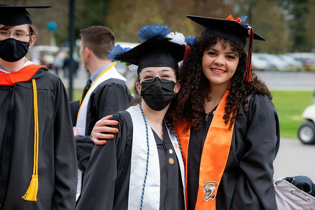 two recent graduates standing outside wearing their regalia.