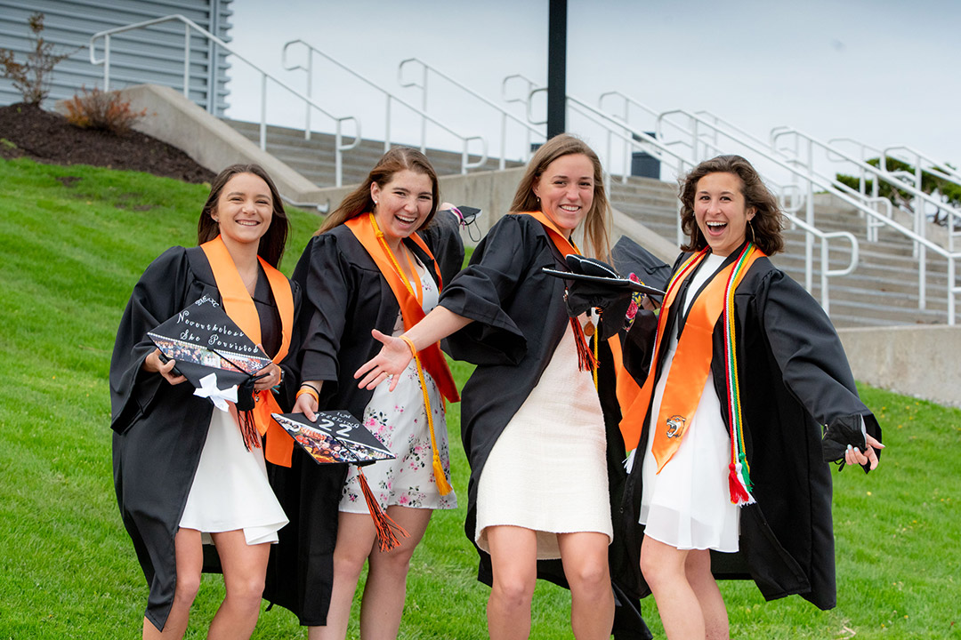 four recent graduates standing outside in their regalia.