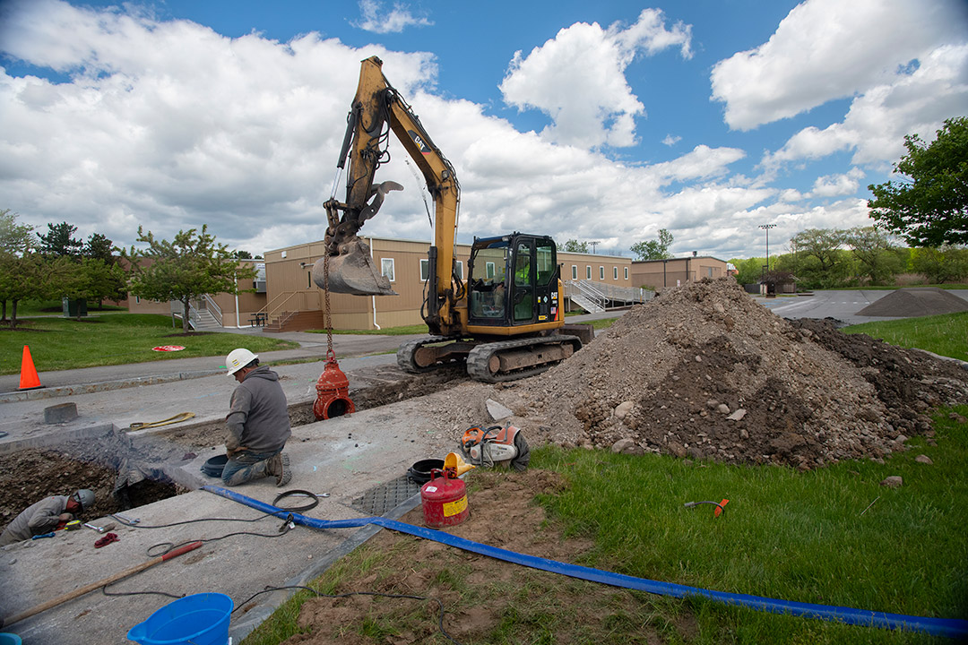 a backhoe digging a trench in a parking lot.