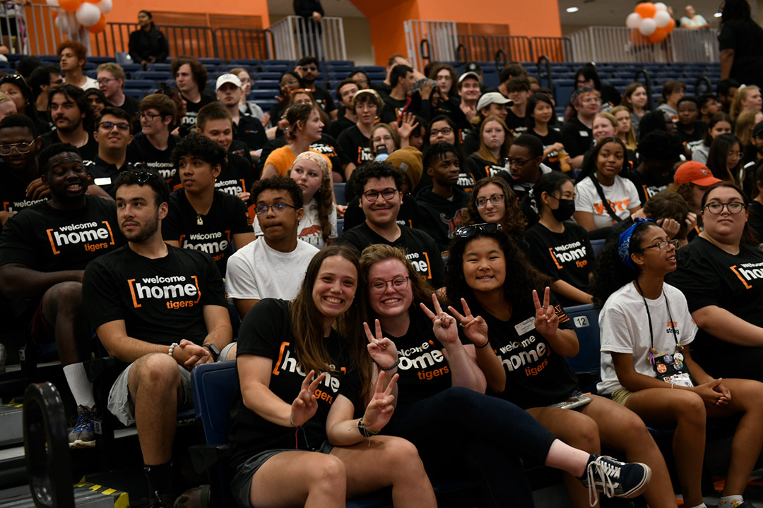 crowd of students sitting in chairs wearing welcome home tigers T-shirts.