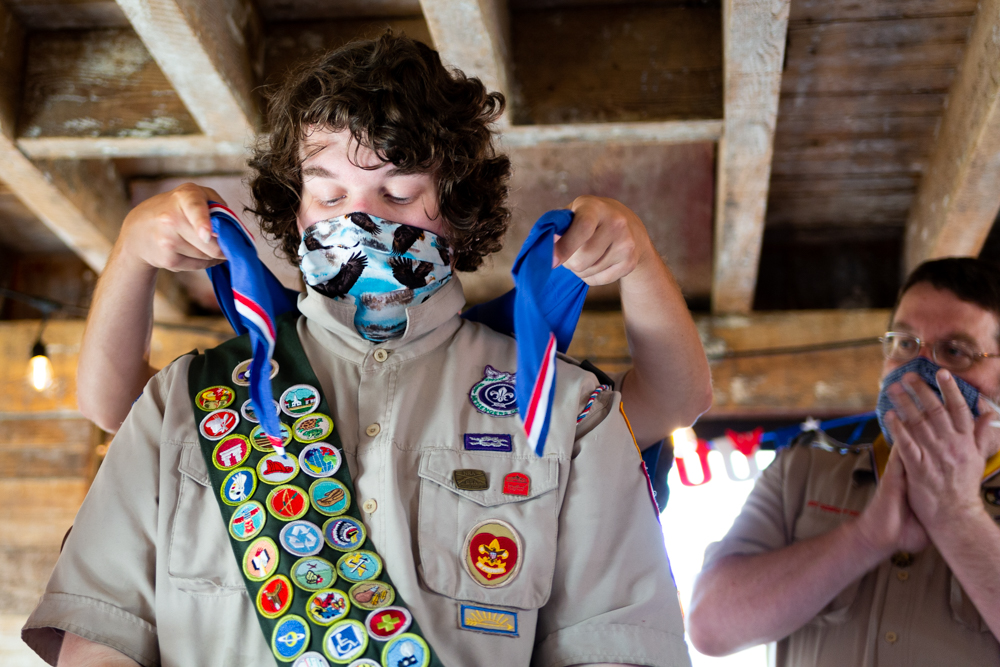 A Boy Scout wearing numerous badges has a sash placed over him.