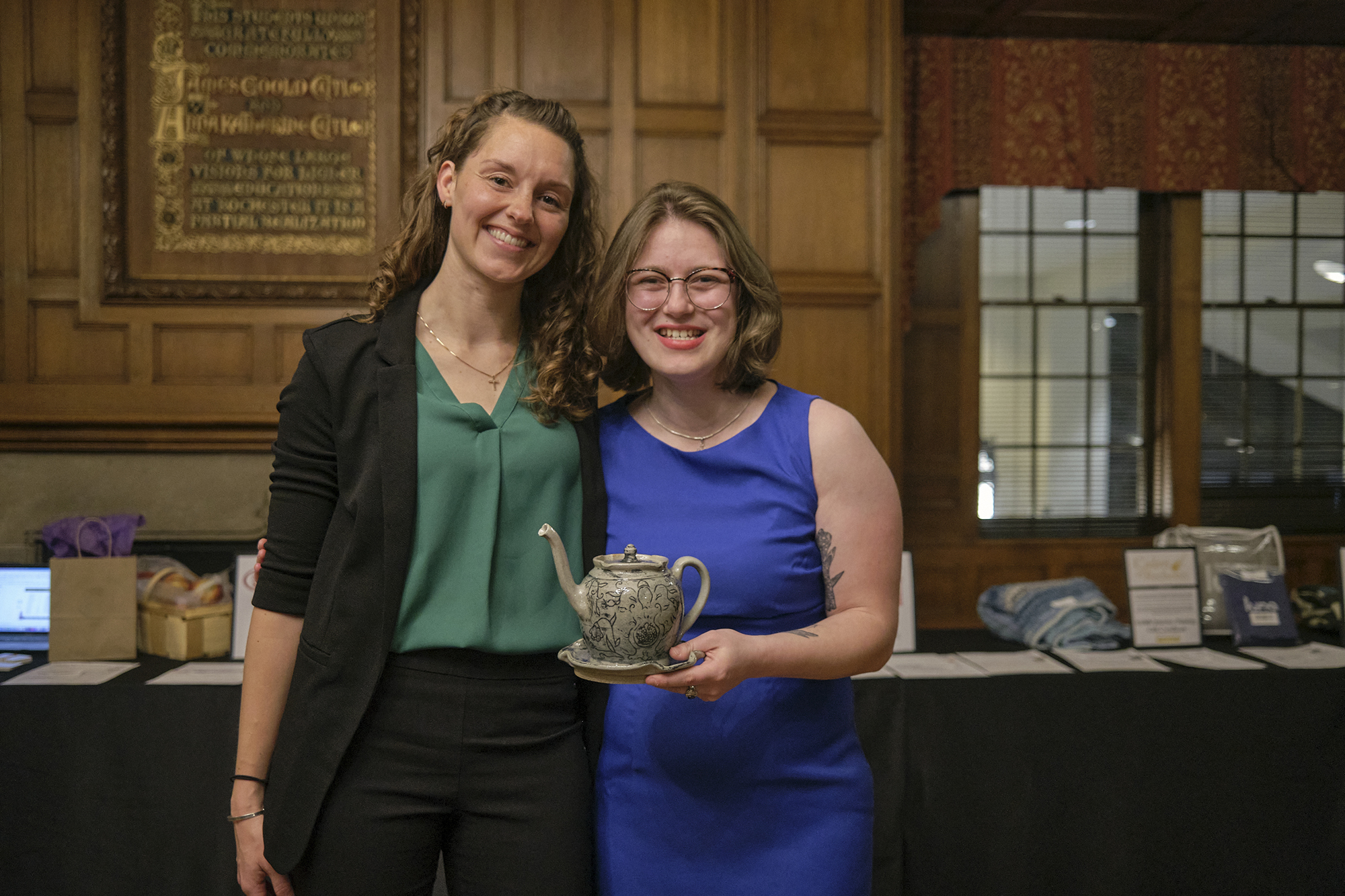 Emma Herz holds one of her teapots while standing next to another person.