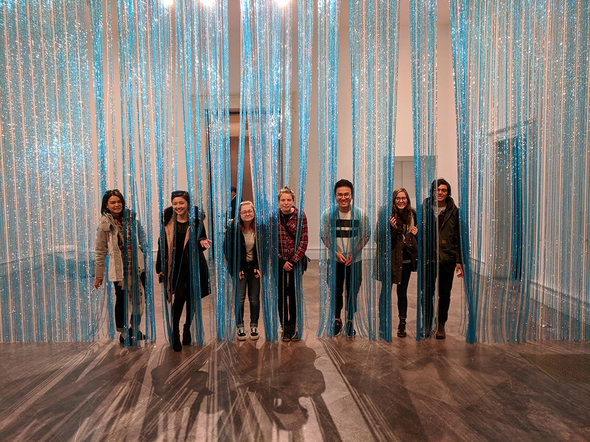 Seven students peek through an art installation that hangs from a ceiling.