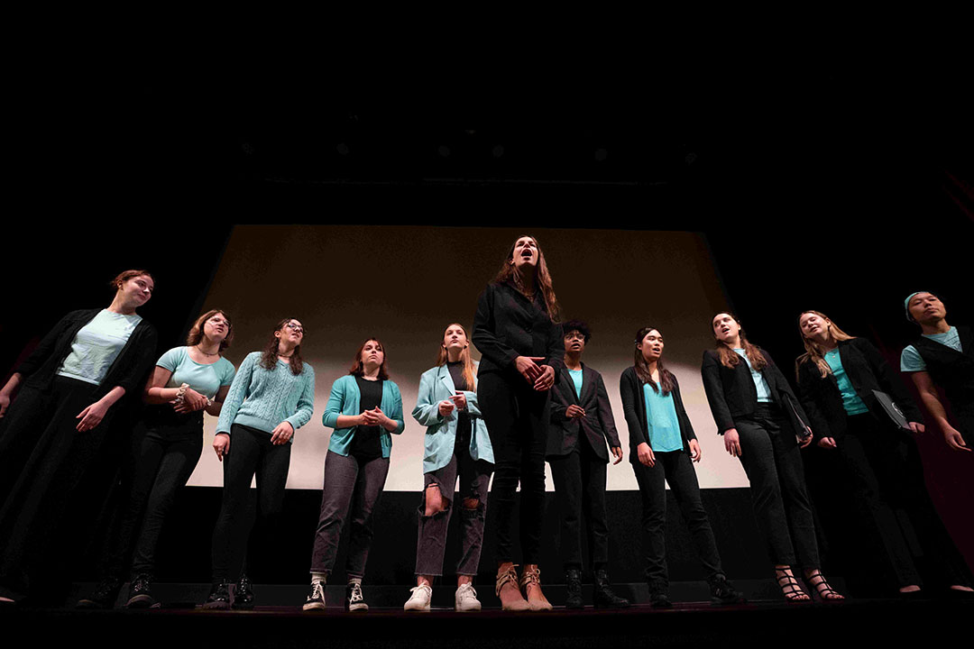 11 college students standing in a semi-circle on a staging, singing.