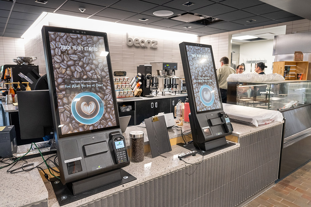 a coffee shop counter with two large screens for placing orders.