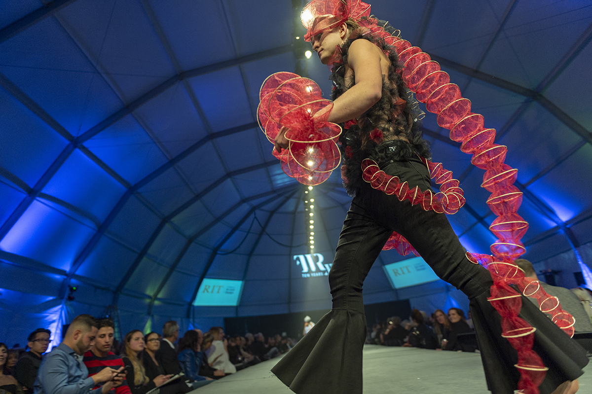 A student walks with a purpose on the runway while donning a black, red and gold piece.