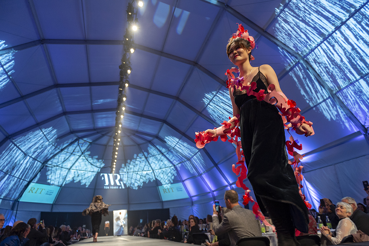 A student smiles while showcasing a fashion design on the Fashion Week runway.