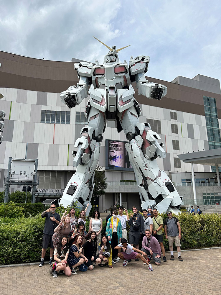 college student posing with a giant robot statue outside in Japan.