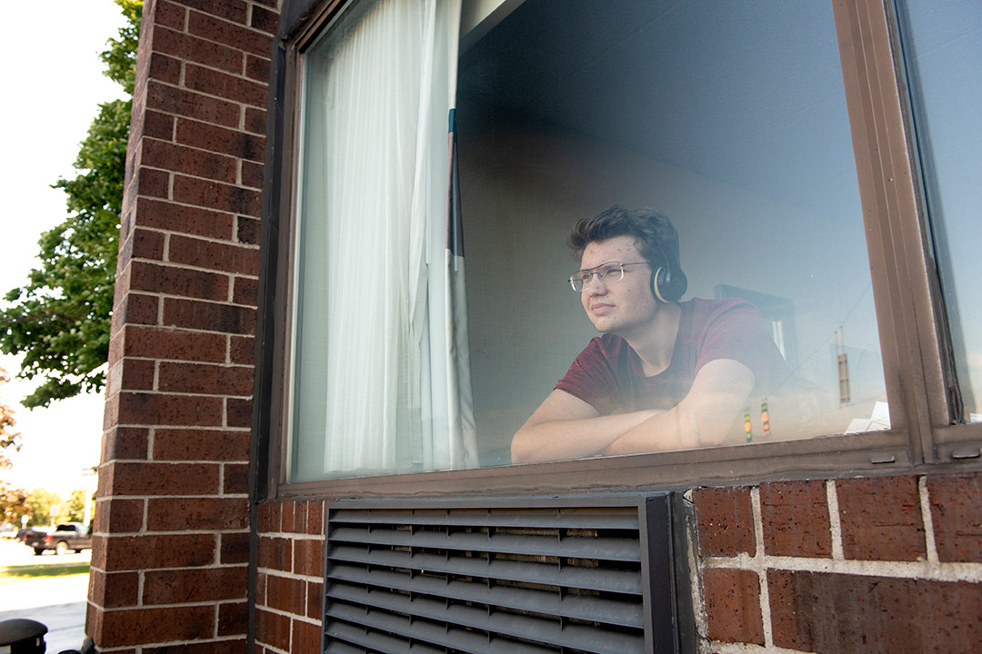 student looking out a hotel room window.