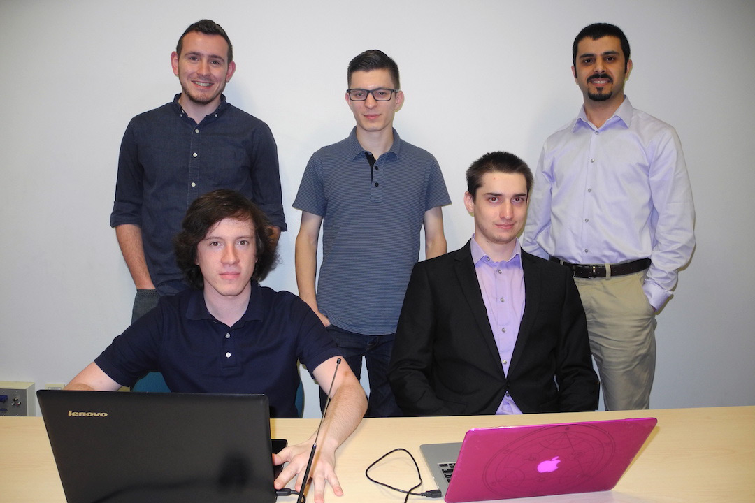 Students and professor pose around table with two computers.